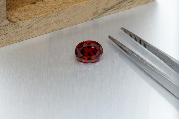 Macro mineral faceted stone Garnet with tweezers on a gray background