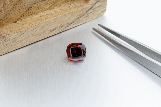 Macro mineral faceted stone Garnet with tweezers on a gray background