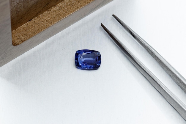 Macro mineral faceted stone sapphire with tweezers on a gray background