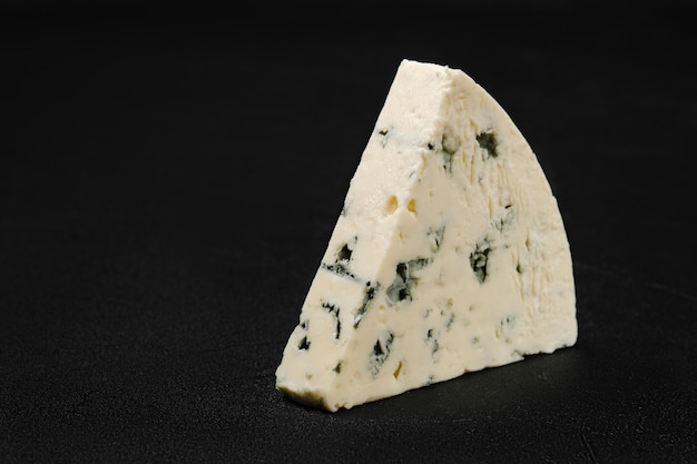 Macro photo of piece of cheese with blue mold on black background