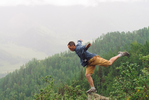 Mad tourist on mountain peak. Joyful traveler stands on one leg over abyss. 