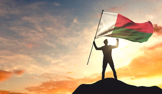 Madagascar flag being waved by a man celebrating success at the top of a mountain 3D Rendering