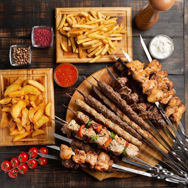 Made dish of skewers, grilled chicken, beef, pork meat with bbq and Tzatziki sauce served with French fries on dark.