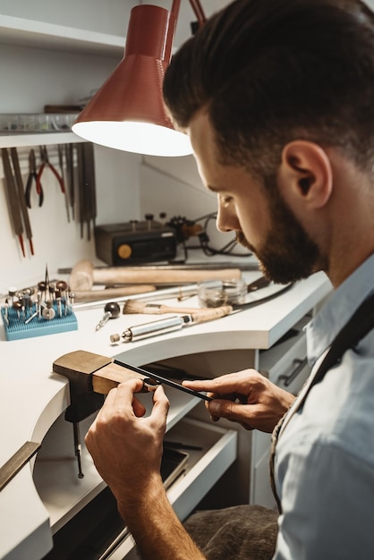 Made with love vertical photo of young male jeweler working and shaping an unfinished ring