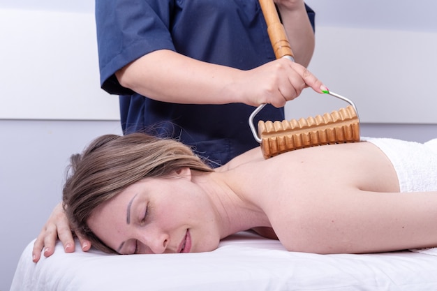 Madero therapy, lymphatic drainage massage - woman having spa back massage in beauty salon using wooden roller massager. Body care concept