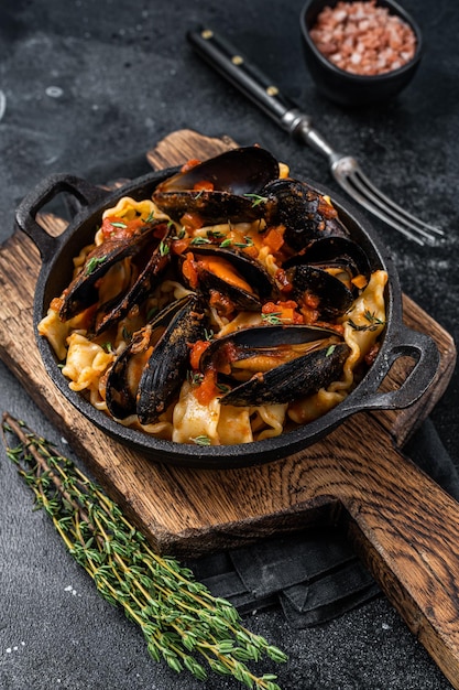 Mafaldine pasta with mussels and tomato sauce. Black background. Top view.