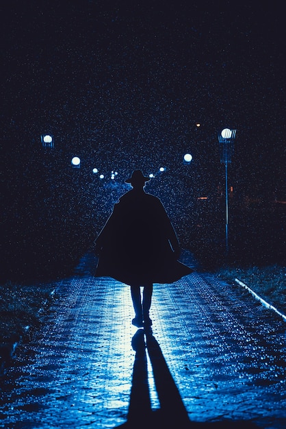 Mafia man in a hat and raincoat at night in a rainy city