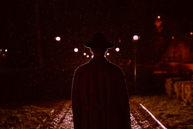 Mafia man in a hat and raincoat at night in a rainy city