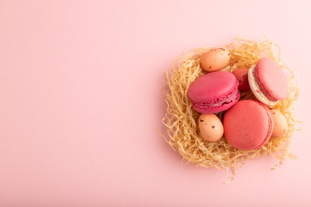 Magenta and pink macaroons and chocolate eggs in decorative paper nest on pink pastel background top view copy space