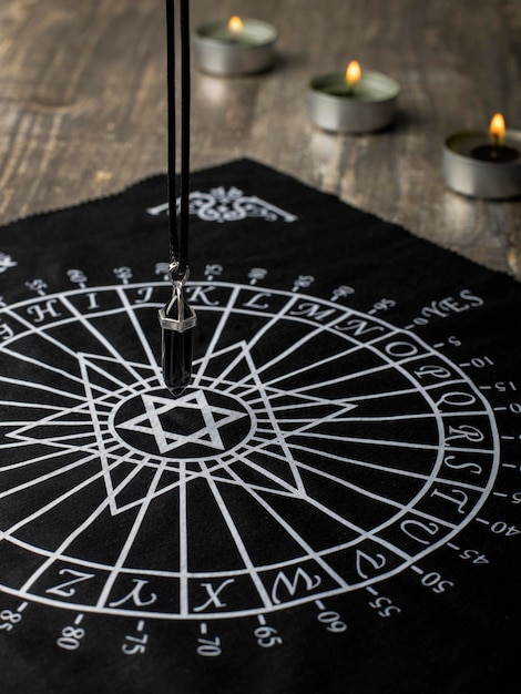 Magical ritual seance divination with a pendulum made of natural stone black agate over a tablecloth for divination closeup