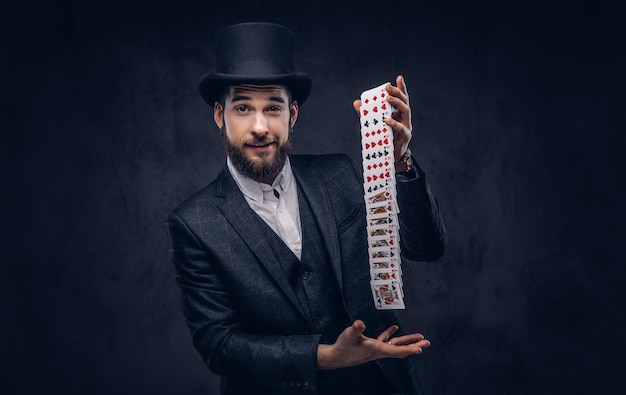 Magician showing trick with playing cards on a dark background.