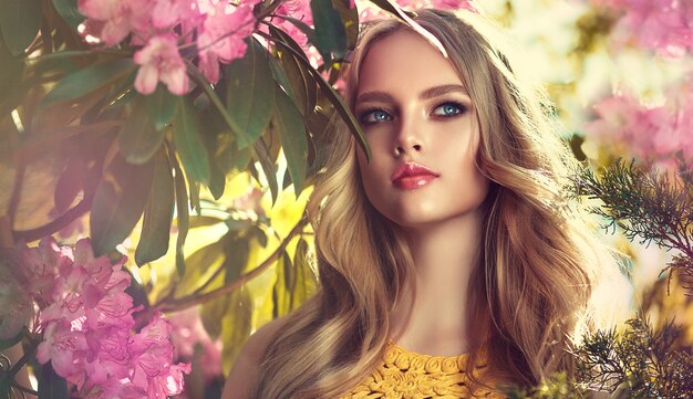 Magnificent young woman surrounded by blossoming flower trees Gentle makeup rose lipstick and freely lying curls 0f long hair Spring style Spring blossom and bloom of youth