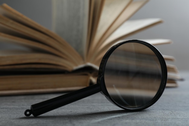 Magnifier and open book on wooden table on light background close up