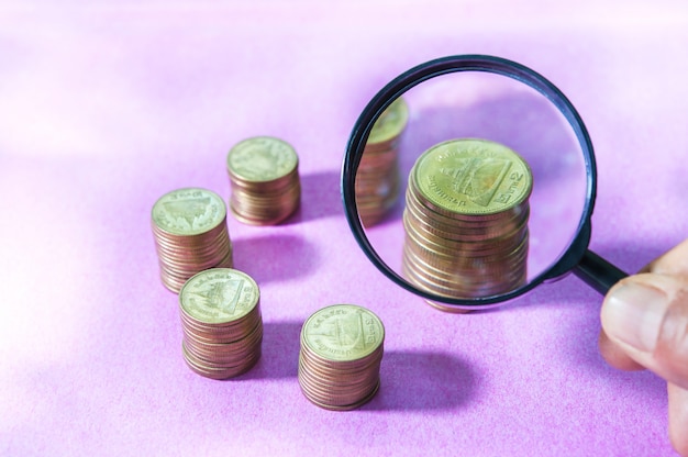 Magnifier searching investment of stacking coin growing on pink background