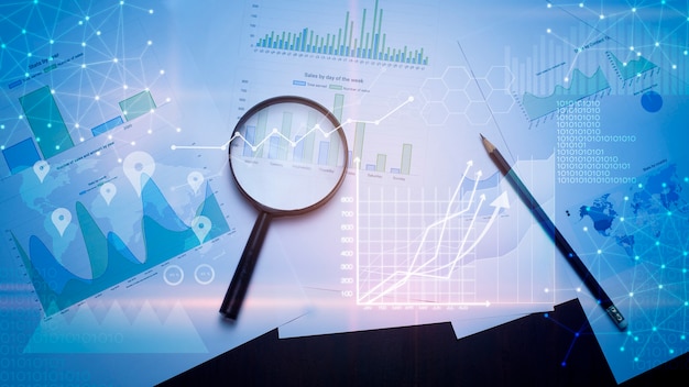 Magnifying glass and documents with analytics data lying on table