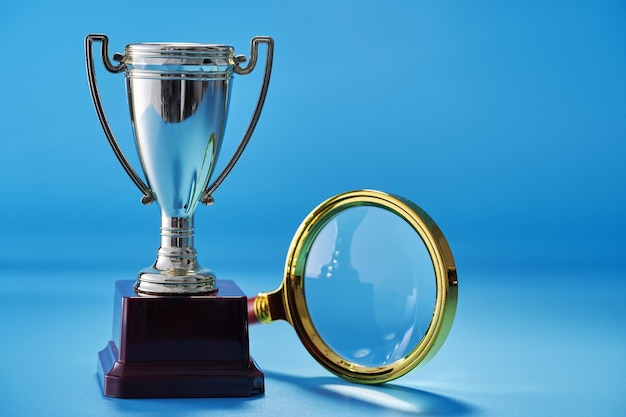 Magnifying glass and the gold colored trophy against blue background