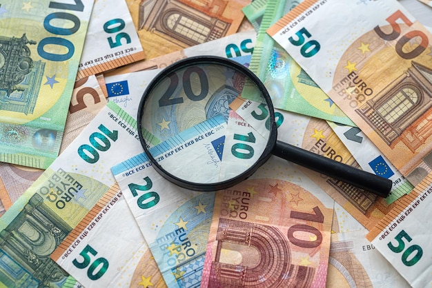 Magnifying glass lie on pile of euro money saving concept