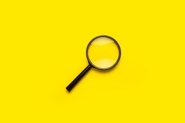 Magnifying glass loupe search symbol on yellow surface with copy space.