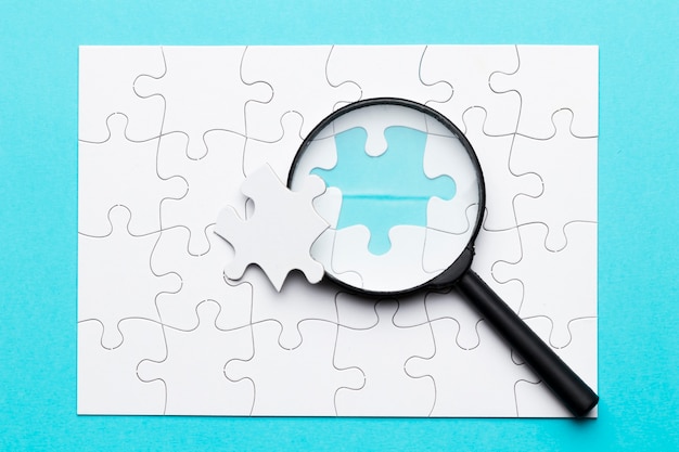 Photo magnifying glass and missing puzzle piece on white grid puzzle on blue surface