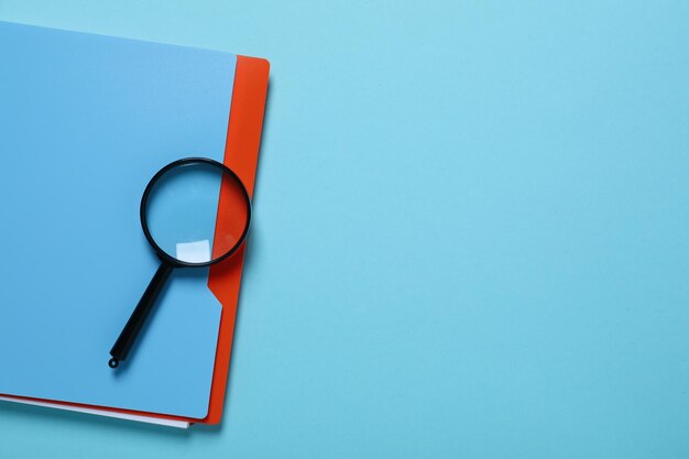 Magnifying glass and notepad on blue background space for text