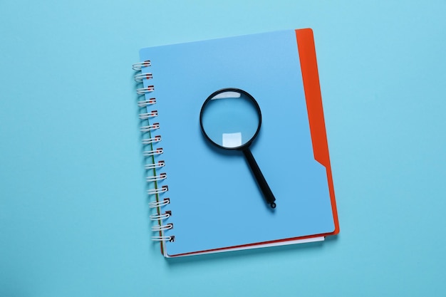 Magnifying glass and notepad on blue background top view