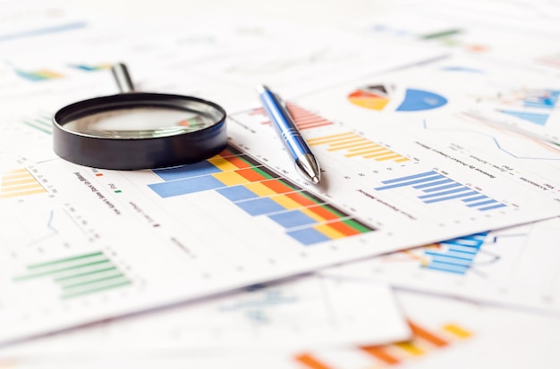 Magnifying glass and pen on financial charts graphs Annual document report