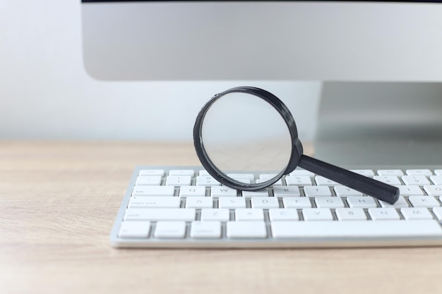 Magnifying glass on wireless keyboard at office desk. Search Engine Optimization concept.