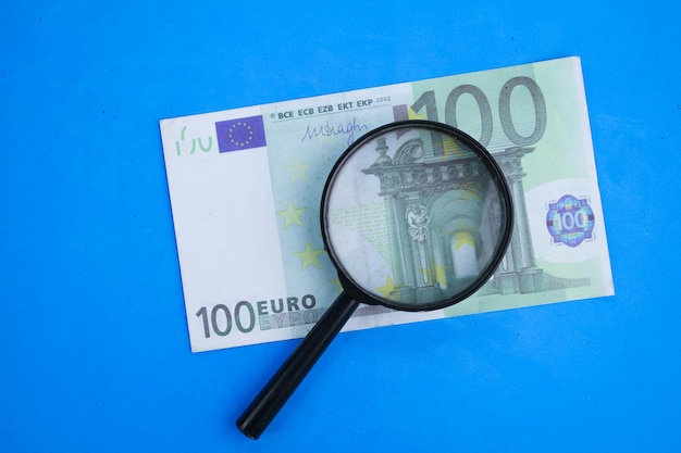 magnifying glass with 100 euros the concept of investing in euros the concept of looking for euro