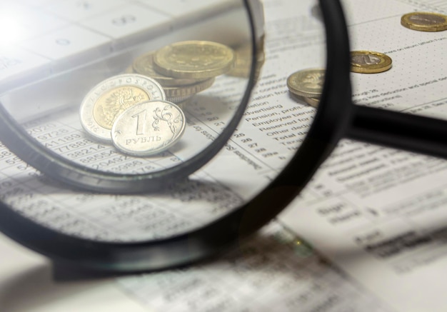 A magnifying glass with coins in the background isolated on an empty white background