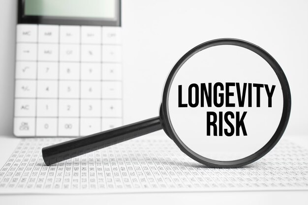 Magnifying glass with text LONGEVITY RISK on white table with calculator