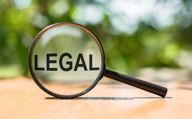 Magnifying glass with word LEGAL on a wooden table over blurred green tree background