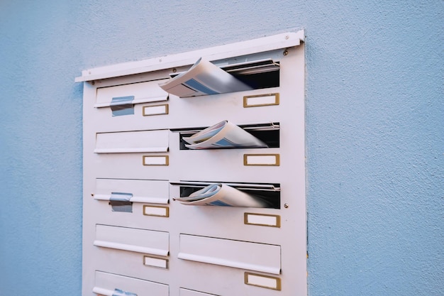 The mailbox of a residential building with daily newspapers sticking out with advertisements and news