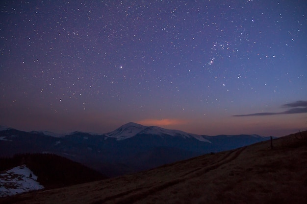 Majestic view of fantastic starry dark sky over magnificent Carpathian mountains covered with evergreen forest and snow-capped peaks in distance. Breathtaking panorama of beauty and magic of nature.