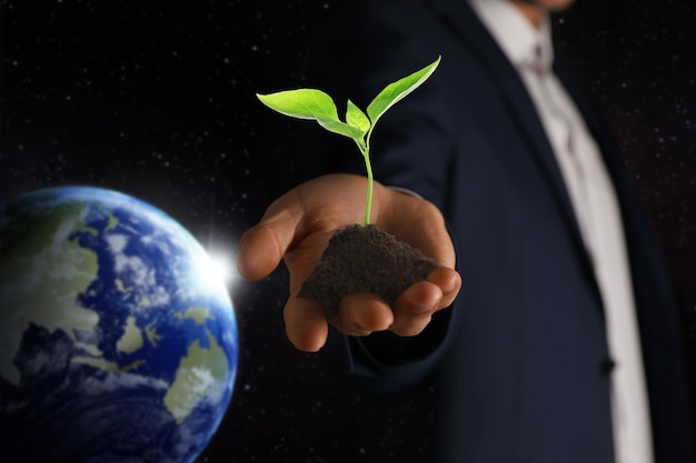 Make Earth green Man holding soil with seedling closeup Black background with globe