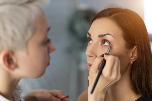 Make-up artist applying bright base color eyeshadow on model's eye 