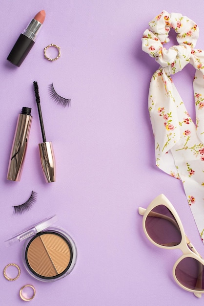 Make up beauty concept Top view vertical photo of scarf scrunchy sunglasses false eyelashes mascara gold rings contouring palette and lipstick on isolated pastel violet background with empty space