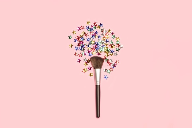 Make up brush with colored stars on a pink background with copy space