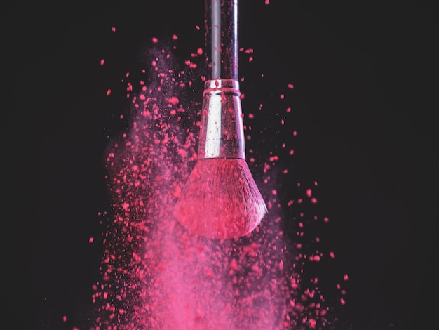 Make-up brush with pink powder explosion on black background