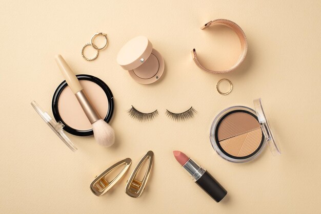 Make up concept Top view photo of circle composition false eyelashes lipstick compact powder brush contouring palette eyeshadow gold wristlet rings and barrettes on pastel beige background