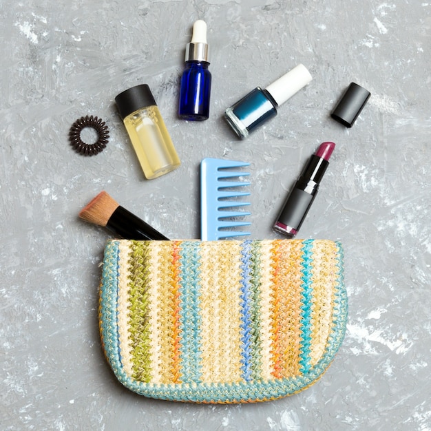 Make up products spilling out of cosmetics bag, on grey cement background with empty