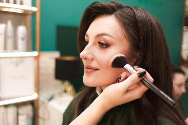 Makeup artist does makeup for a beautiful girl. Woman does face contouring for her client