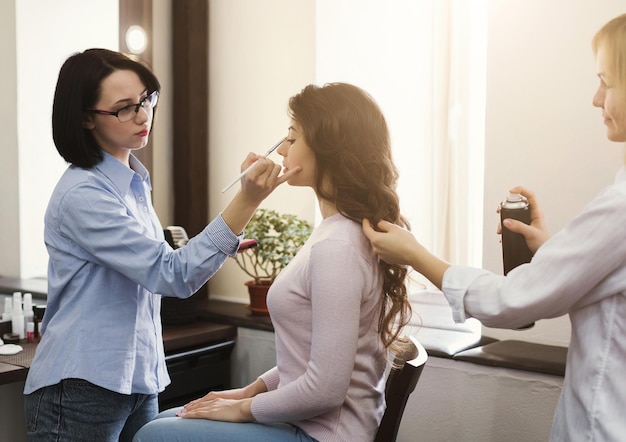 Makeup artist and hairdresser work in tandem, curl and color model in beauty salon