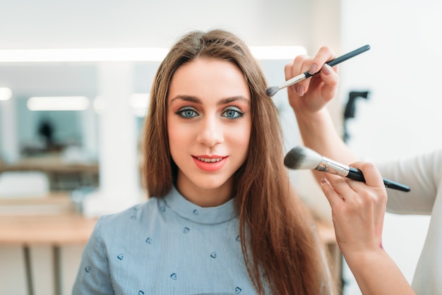 Makeup artist hands with brushes work with cute woman