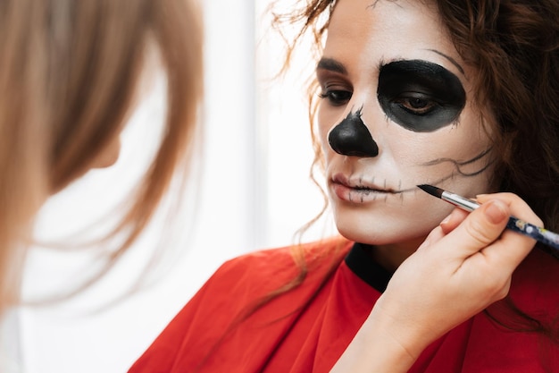 A makeup artist makes up a demon to a young girl in a beauty salon Halloween Celebration Concept