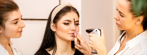 Makeup artist using an airbrush on the face of a young caucasian woman in a beauty salon