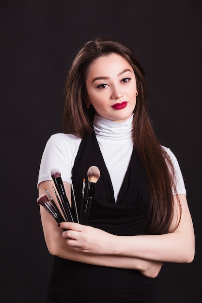 Makeup artist with brushes in hand on a black wall