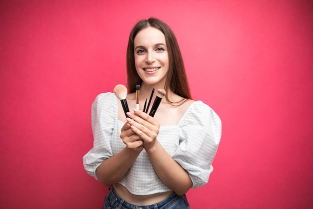 Makeup artist with brushes in hand on a pink background