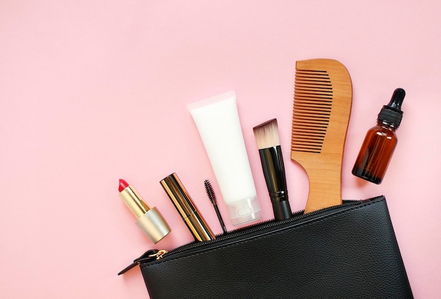 Makeup bag with decorative cosmetics and accessories on pink background