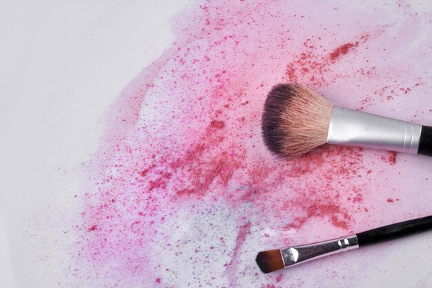 Makeup brush and scattered face powder on white background