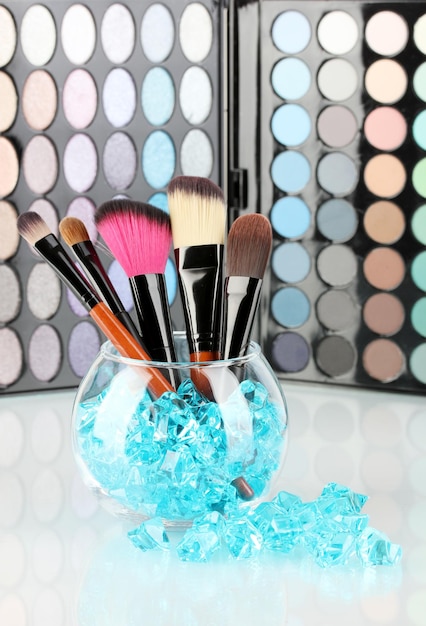 Makeup brushes in a bowl with stones on palette of shadows background